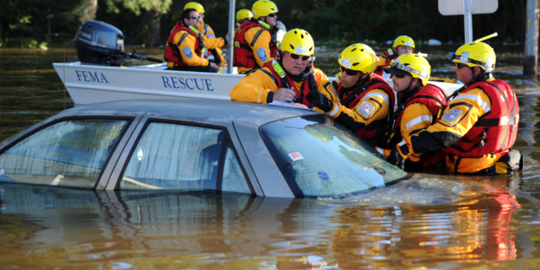 Search and rescue team stand in flooded street mapping their route on top of a car. Another rescue team is seen in the back on a boat