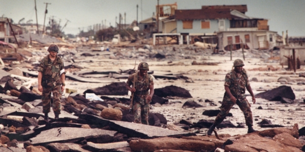 Soldiers from the South Carolina National Guard walk across debris with damaged houses in the background on patrol at Folly beach to protect against looting after Hurricane Hugo.